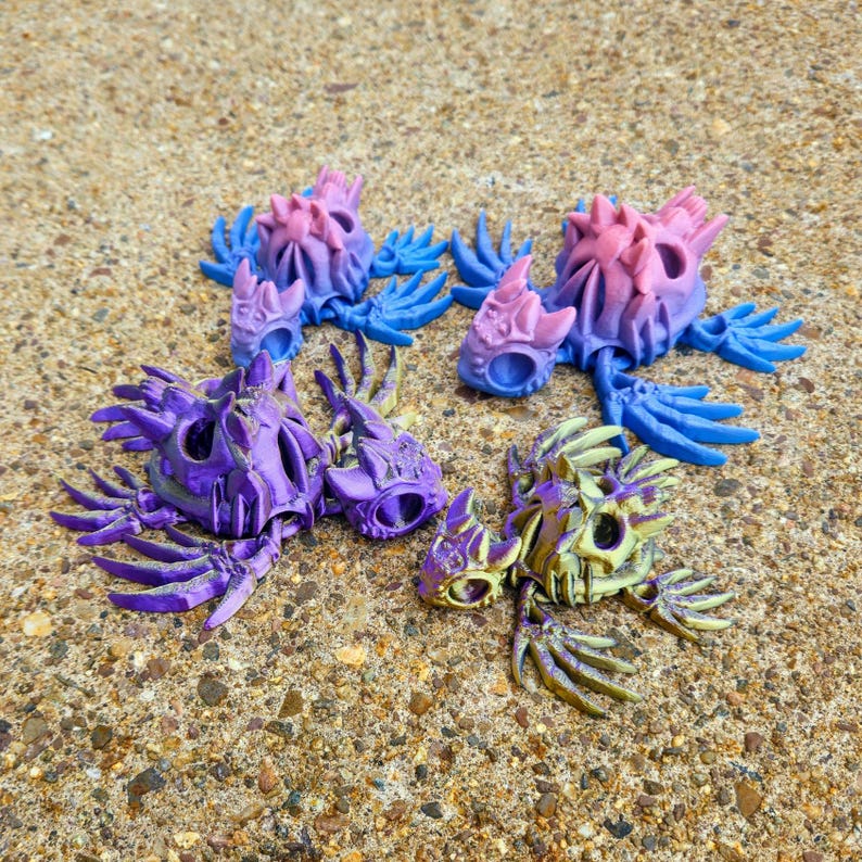 Peut inclure: Quatre cr&eacute;atures squelettiques color&eacute;es en plastique. Les cr&eacute;atures sont dans diff&eacute;rentes poses avec des ailes et des queues. Les cr&eacute;atures sont peintes dans des tons de violet, bleu, rose et jaune.