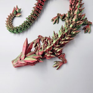 May include: A 3D printed dragon figurine with a red and green iridescent finish. The dragon is curled in a serpentine pose with its head raised and its wings spread.