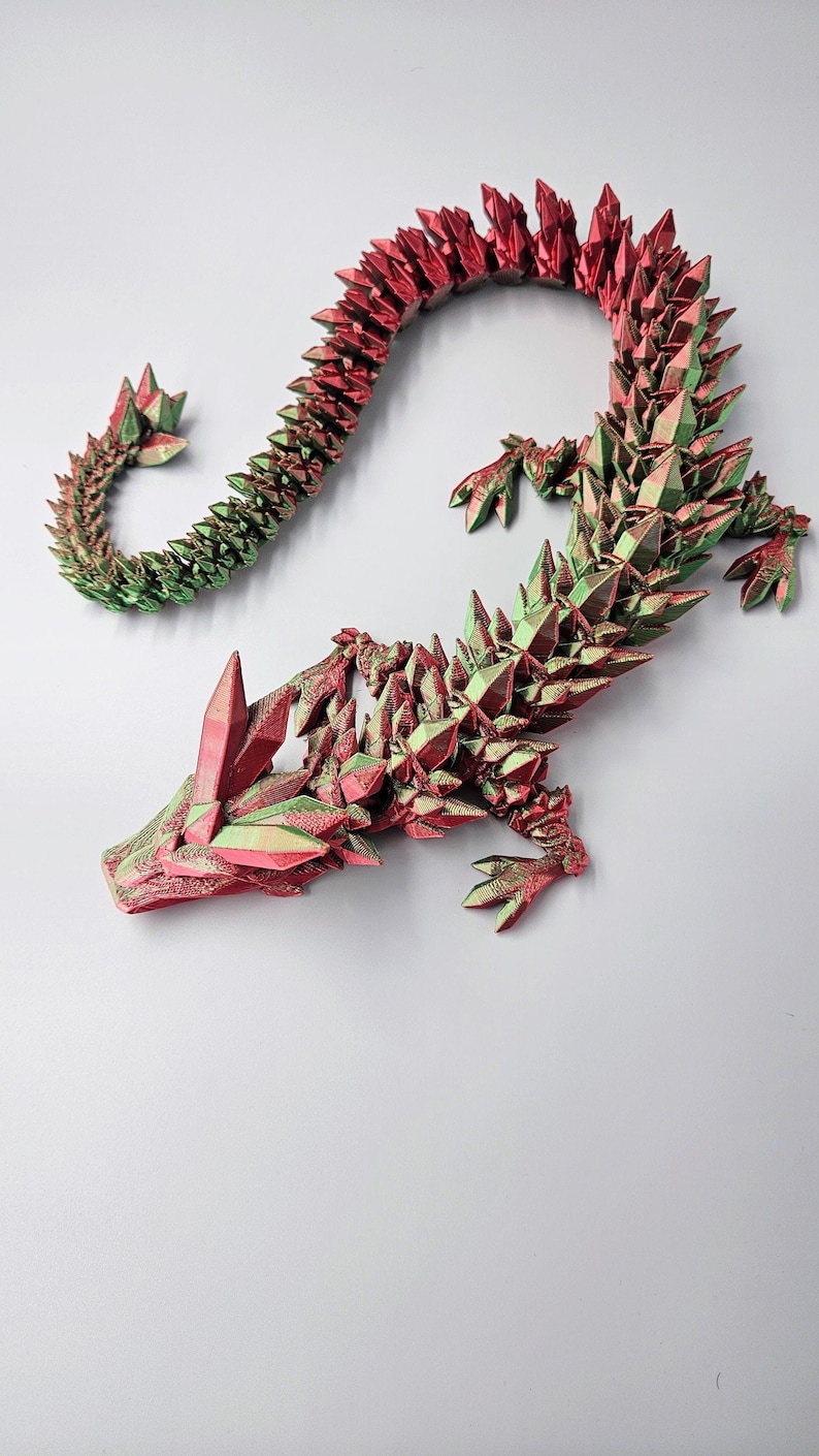 May include: A 3D printed dragon figurine with a red and green iridescent finish. The dragon is curled in a serpentine pose with its head raised and its wings spread.