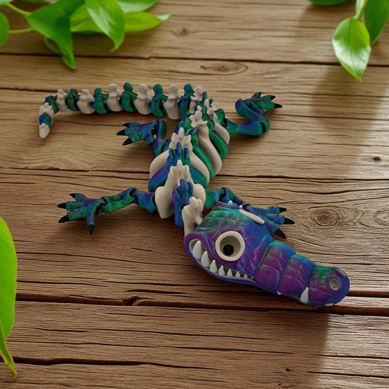 Pu&ograve; includere: Una colorata scultura di alligatore articolata realizzata in argilla. L'alligatore presenta una testa viola, blu e verde con denti bianchi e un grande occhio. Il corpo &egrave; un mix di verde, blu e bianco, con una spina dorsale segmentata.