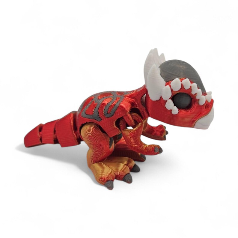May include: A red and gray 3D-printed dinosaur figurine with a detailed design. The figurine has a segmented tail, gold-colored feet, and white horns. The dinosaur's head is gray with white accents around the eyes.