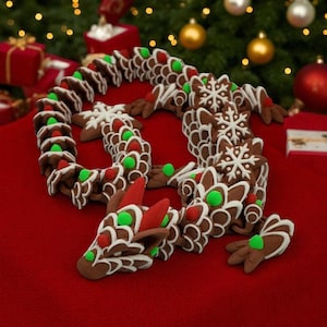 May include: A gingerbread dragon with brown, white, red, and green icing details. The dragon is decorated with snowflake and dot designs. The dragon is on a red surface with a Christmas tree and ornaments in the background.