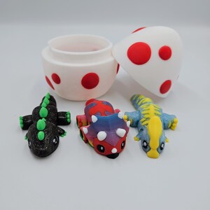 May include: A set of three small dinosaur toys, including a black and green dinosaur, a multi-colored dinosaur, and a blue and yellow dinosaur. The dinosaurs are sitting inside a white egg-shaped container with red polka dots.