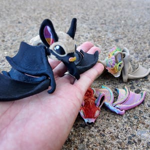 May include: A collection of four small, hand-painted bat figurines. The bats are made of a variety of materials, including ceramic, resin, and fabric. The bats are painted in a variety of colors, including black, white, brown, pink, and blue. The bats are all different sizes and shapes.