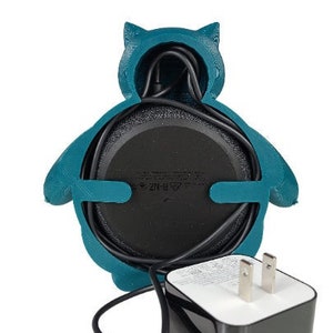 May include: A teal blue 3D printed owl-shaped holder for a smart speaker with a black power cord and a black power adapter.