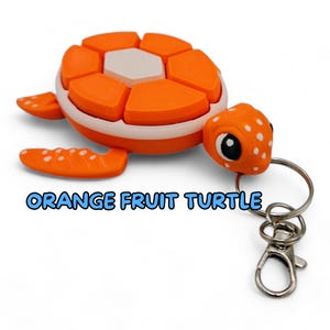 May include: Orange fruit turtle keychain with a white shell and black eyes. The turtle is made of plastic and has a white and orange color scheme. The keychain has a silver metal ring and a silver metal clasp.
