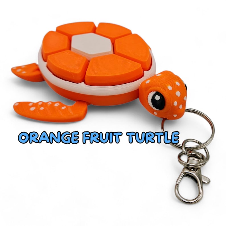 May include: Orange fruit turtle keychain with a white shell and black eyes. The turtle is made of plastic and has a white and orange color scheme. The keychain has a silver metal ring and a silver metal clasp.