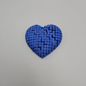 May include: A blue heart-shaped object composed of numerous small, square blocks. The heart has a textured appearance and is set against a plain, light background. The design gives a 3D effect.