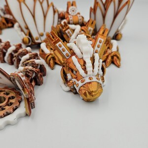 May include: A 3D printed steampunk dragon figurine painted in gold and white. The dragon features intricate details, including gears, wings, and a crown.