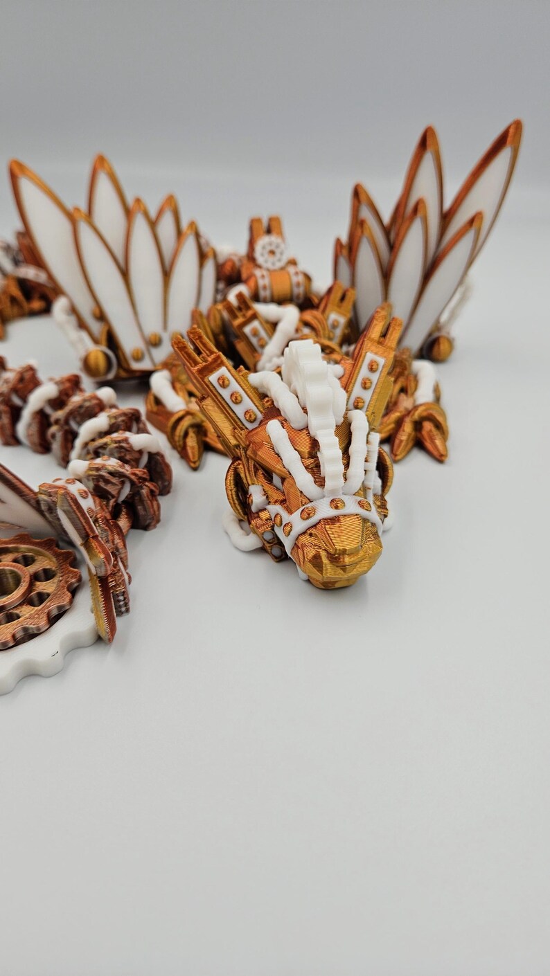 May include: A 3D printed steampunk dragon figurine painted in gold and white. The dragon features intricate details, including gears, wings, and a crown.