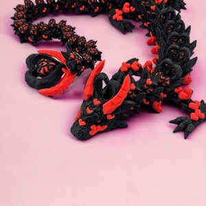 Op de afbeelding: Een zwart en rood 3D-geprint drakenbeeldje met een hartvormig ontwerp. De draak is opgerold in een cirkel met zijn kop op zijn staart.