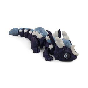 May include: A dark blue articulated dragon figurine with light blue and white accents. The dragon has a segmented body, with cloud-like details and star-shaped embellishments. The eyes are large and detailed.