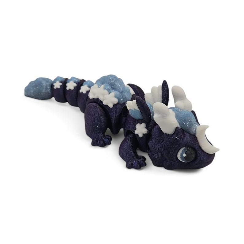 May include: A dark blue articulated dragon figurine with light blue and white accents. The dragon has a segmented body, with cloud-like details and star-shaped embellishments. The eyes are large and detailed.
