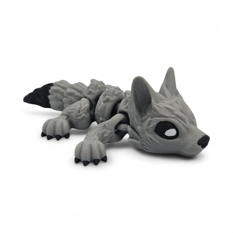 Peut inclure: Figurine de loup articul&eacute; gris avec une queue &agrave; bout noir. Le loup a une surface textur&eacute;e et d&eacute;taill&eacute;e et est pos&eacute; allong&eacute;. Les yeux sont noirs avec des reflets blancs et le nez est noir.
