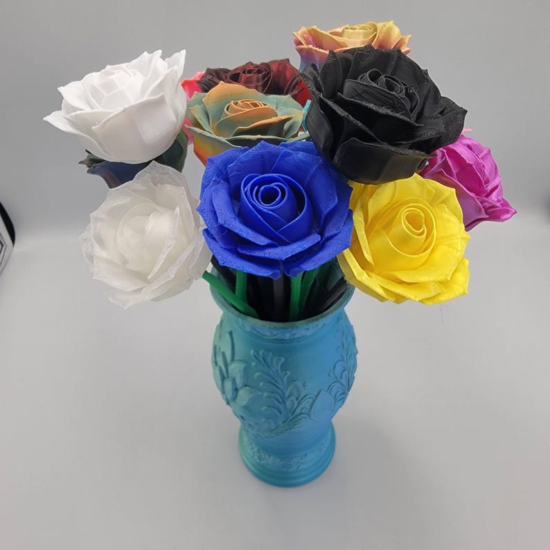 May include: A bouquet of colorful artificial roses in a light blue vase. The roses are in various colors, including white, blue, yellow, black, and pink. The vase has a decorative floral pattern.