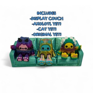 Puede incluir: Un sof&aacute; de exhibici&oacute;n turquesa con tres figuras de Yeti coloridas. Las figuras incluyen un Axolotl Yeti, un Cat Yeti y un Original Yeti. El texto de la imagen dice "Includes -Display Couch -Axolotl Yeti -Cat Yeti -Original Yeti."
