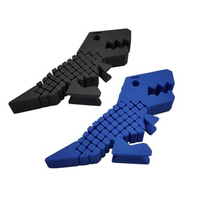 Puede incluir: Dos topes de puerta con forma de dinosaurio. Uno es negro, el otro azul. Cada tope de puerta est&aacute; hecho de peque&ntilde;os bloques cuadrados, lo que les da una apariencia texturizada. Las mand&iacute;bulas del dinosaurio est&aacute;n abiertas y la cola est&aacute; en &aacute;ngulo.