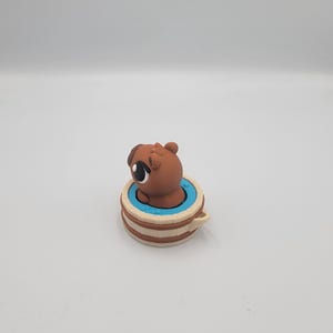 May include: A brown pug figurine peeks out of a light blue and tan teacup. The pug has large, expressive eyes and a small, rounded head. The teacup has a handle and a layered design.