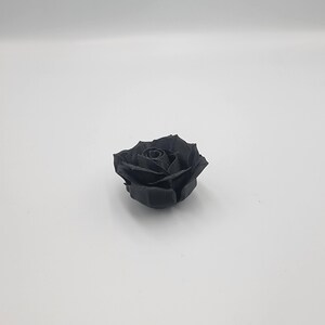 May include: A single, fully bloomed black rose, centered against a white background. The rose's petals are intricately detailed, showcasing a realistic floral design. The dark color of the rose provides a striking contrast against the bright backdrop.