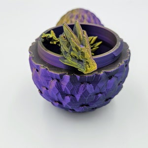May include: A purple dragon egg-shaped trinket box with a gold dragon head on top. The box is made of 3D printed plastic.