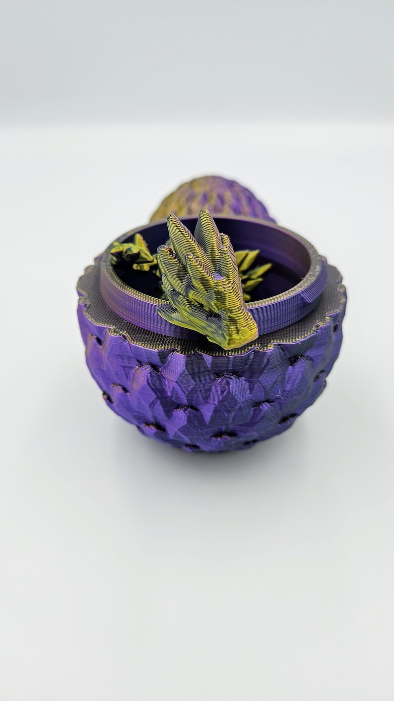 May include: A purple dragon egg-shaped trinket box with a gold dragon head on top. The box is made of 3D printed plastic.