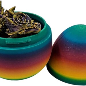 May include: A rainbow egg-shaped container with a lid that opens to reveal a small, gold-coloured dragon figurine inside.