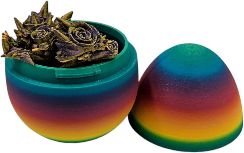 May include: A rainbow egg-shaped container with a lid that opens to reveal a small, gold-coloured dragon figurine inside.