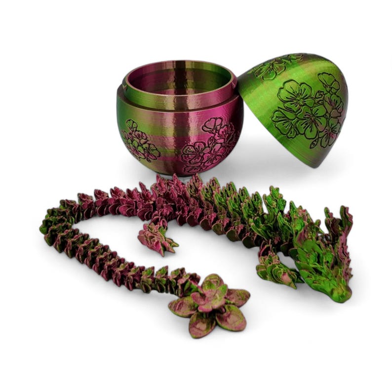 Pu&ograve; includere: Una statuetta di drago iridescente verde e rosa con un contenitore a forma di uovo abbinato. Il drago &egrave; in plastica e presenta un design dettagliato. Il contenitore a forma di uovo &egrave; aperto e presenta un motivo floreale.