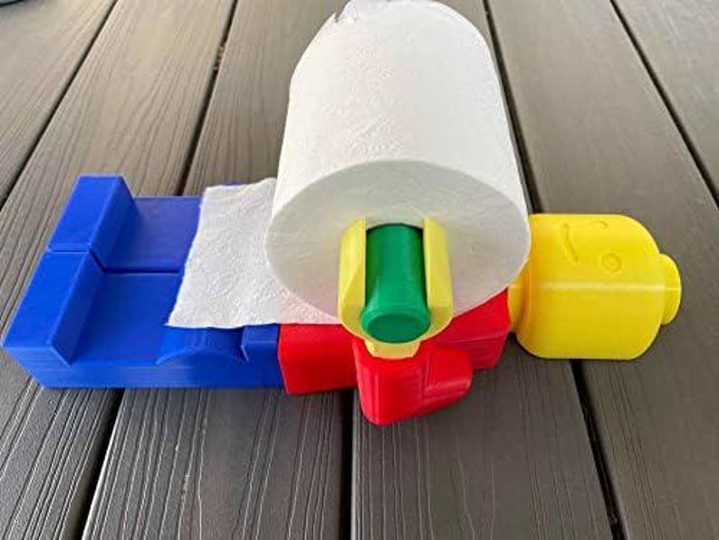K&ouml;nnte beinhalten: Ein blau, rot, gelb und gr&uuml;n gef&auml;rbter Papierhandtuchhalter mit einer Rolle wei&szlig;er Papierhandt&uuml;cher. Der Halter hat ein gelbes, kopff&ouml;rmiges Teil an der Seite.