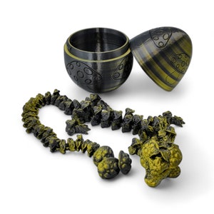 May include: A black and gold egg-shaped container with a lid, open to reveal a chain of small black and gold mushroom-shaped charms.
