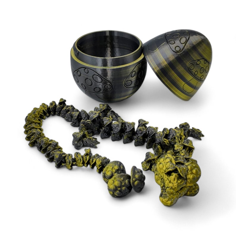 May include: A black and gold egg-shaped container with a lid, open to reveal a chain of small black and gold mushroom-shaped charms.