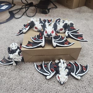 May include: A collection of small, bat-shaped figurines. The bats have white bodies, black wings with red accents, and red eyes. They are arranged on a brown surface and a gray carpet.