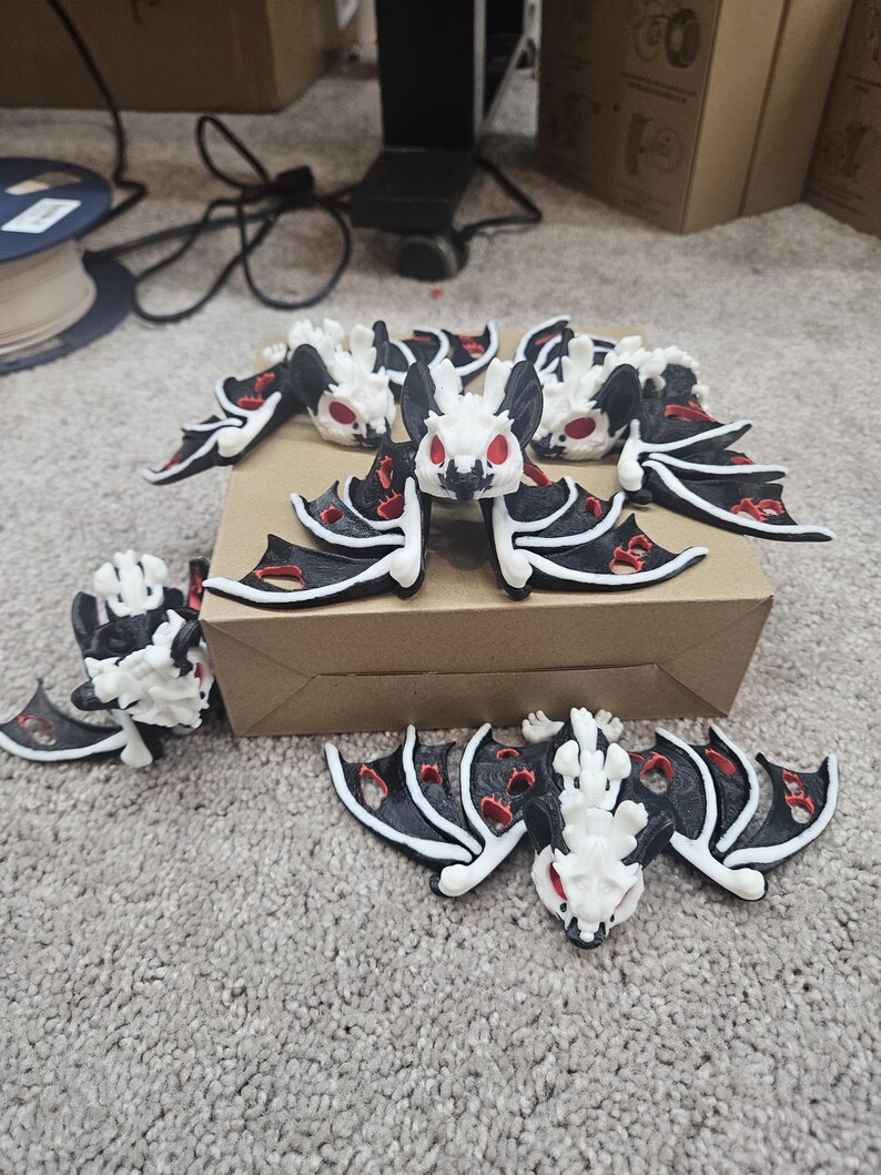 May include: A collection of small, bat-shaped figurines. The bats have white bodies, black wings with red accents, and red eyes. They are arranged on a brown surface and a gray carpet.