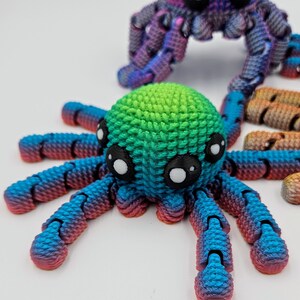 Op de afbeelding: Twee kleurrijke 3D-geprinte octopus speelgoedjes. E&eacute;n is blauw, groen en roze, de andere is paars en blauw. Beide hebben grote zwarte ogen.