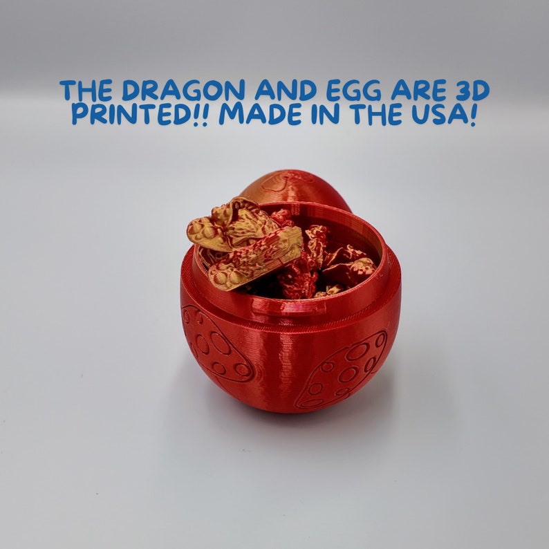 May include: A red 3D printed egg with a golden dragon figurine inside. The egg has a textured surface with a repeating pattern. The text "THE DRAGON AND EGG ARE 3D PRINTED!! MADE IN THE USA!" is displayed above the egg.
