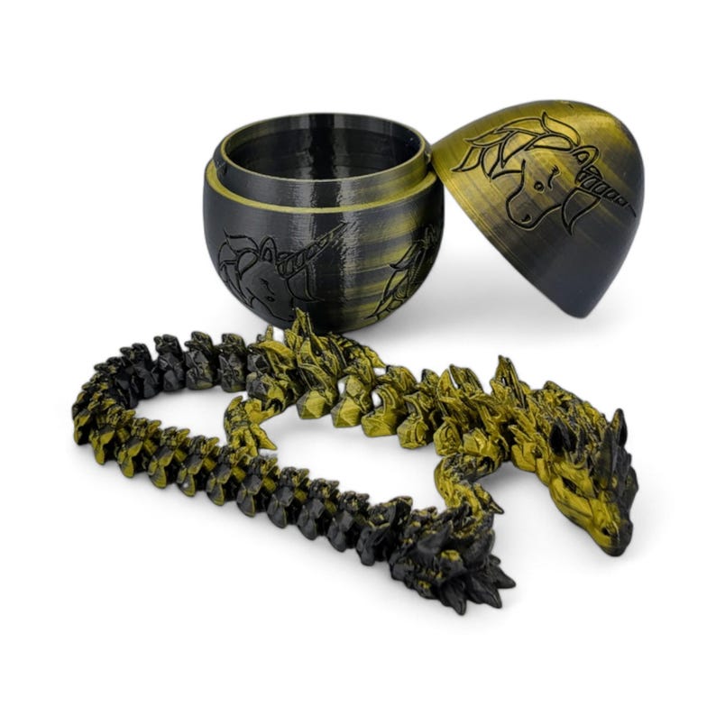 May include: A gold and black dragon-shaped puzzle with a unicorn design on the lid. The puzzle is made of plastic and is in the shape of a dragon. The lid is in the shape of an egg and has a unicorn design on it.