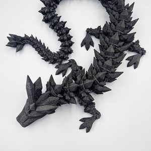 May include: A black, 3D printed dragon sculpture with a spiky, crystalline texture. The dragon is curled in a circle with its head resting on its tail.