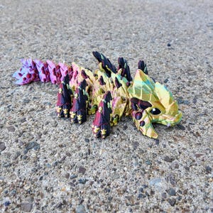 May include: A multi-colored origami dragon with iridescent scales. The dragon is made of paper and has a long tail and a head with a pointed snout.