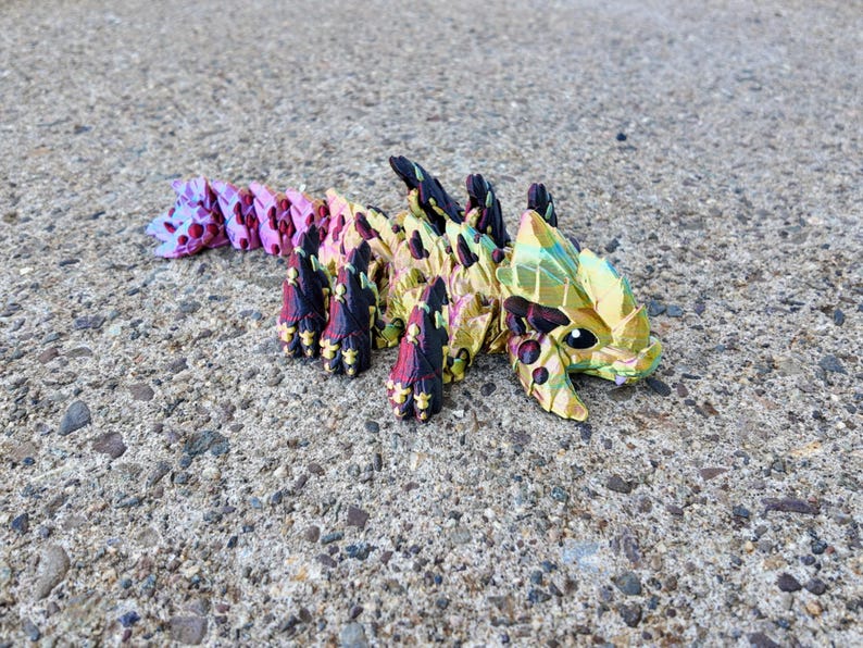May include: A multi-colored origami dragon with iridescent scales. The dragon is made of paper and has a long tail and a head with a pointed snout.