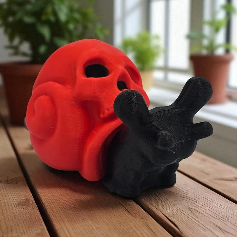 May include: A red skull-shaped sculpture with a black, stylized hand emerging from its mouth. The sculpture is made of a solid material and sits on a wooden surface. The design is a unique, artistic representation.