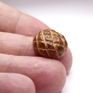 Puede incluir: Un pequeño pan tallado con una corteza marrón dorada y un patrón de trama cruzada. Este artículo en miniatura es probablemente un elemento decorativo o un accesorio para casas de muñecas. El diseño detallado le da un aspecto realista.