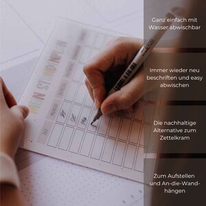 May include: A white dry-erase weekly planner with the words "EIN STUNDENPLAN" at the top. The planner is divided into days of the week and time slots. A hand is writing on the planner with a black marker.