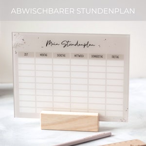 May include: A white dry-erase weekly schedule board with the text "Mein Stundenplan" at the top. The board is divided into columns for each day of the week: Monday, Tuesday, Wednesday, Thursday, and Friday. The board is on a wooden stand.