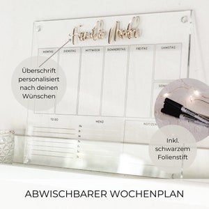 Könnte beinhalten: Ein transparenter Acryl-Wochenplaner mit einer goldenen Aufschrift "Familie Wochen". Der Planer hat Abschnitte für jeden Tag der Woche, einschließlich Montag, Dienstag, Mittwoch, Donnerstag, Freitag, Samstag und Sonntag. Der Planer hat auch Abschnitte für "To Do", "Menü" und "Notizen". Der Planer wird mit einem schwarzen Trockenlöschmarker geliefert.