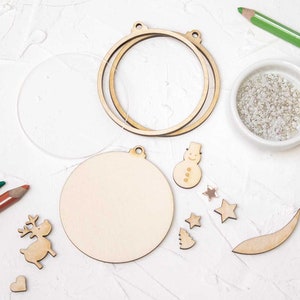 Könnte beinhalten: Ein Bastelset zum Herstellen von Weihnachtsbaumschmuck. Das Set enthält einen Holzschmuck, einen Schneemann, ein Rentier, einen Stern, einen Baum, einen Halbmond und eine Perlenkette.