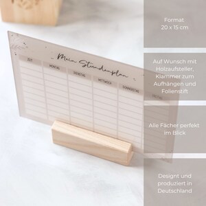 May include: A clear acrylic weekly planner with a light brown wood stand. The planner has a floral design and the text "Mein Stundenplan" at the top. The planner measures 20 x 15 cm.