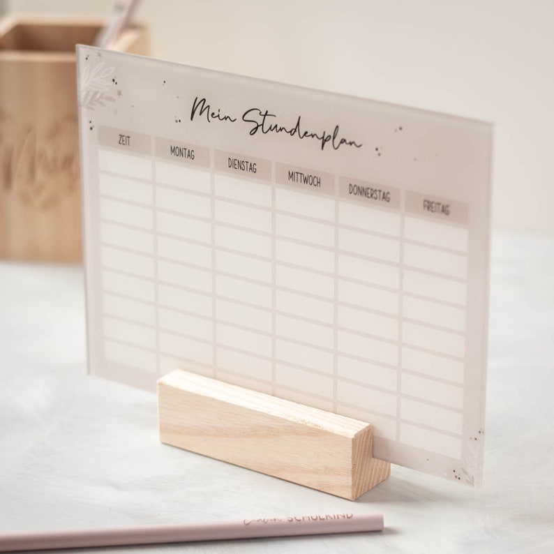 May include: A white acrylic dry erase board with a light brown wood stand. The board has a grid pattern and the text "Mein Stundenplan" at the top. The board is used for scheduling.