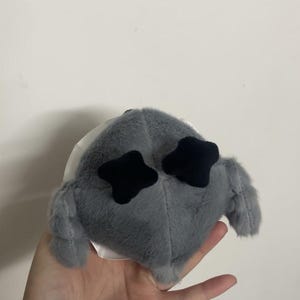 May include: Gray plush toy with black star-shaped eyes. The toy has a round body and two small, furry arms.