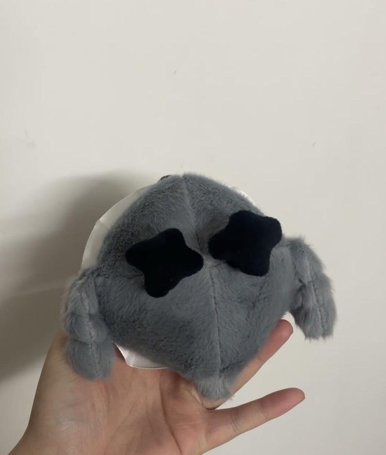 May include: Gray plush toy with black star-shaped eyes. The toy has a round body and two small, furry arms.