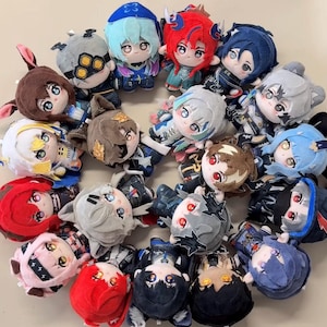 Puede incluir: Una colección de veintiuna pequeñas muñecas de peluche suaves dispuestas en un patrón circular. Cada muñeca presenta colores de cabello distintos, incluyendo rojo, azul, marrón, gris y negro, junto con expresiones faciales bordadas y trajes de tela detallados.